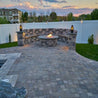 Stone fire pit and seating area at dusk, surrounded by a paved patio.
