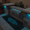 Waterfall feature with LED lighting, flowing into a stone-filled basin at night.
