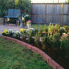 Curved red brick garden edging bordering lush flowers and green lawn.
