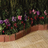 Red brick garden edging bordering vibrant pink, purple, and red flowers on a beige stone patio.
