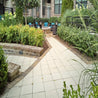Off-white square pavers create a tranquil patio pathway, bordered by lush greenery and brick accents.
