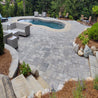 Grey stone patio pavers surrounding a pool, landscaping with pine straw and rocks.
