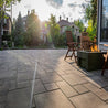 Large grey rectangular patio stones create a sun-drenched backyard oasis with fire pit and chairs.
