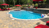 Swimming pool with stone coping, surrounded by patio pavers and red lounge chairs.

