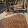 Outdoor patio scene with multi-toned brick paving stones; a person sits at a cafe table.
