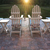 Patio chairs facing sunset over tranquil lawn, situated on a brick paver patio.
