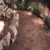Curved brick pathway at night, bordered by landscaping and a fire pit.
