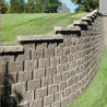 Curved retaining wall made of gray textured blocks, set against a grassy landscape.

