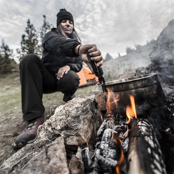 Person using a multi-tool to cook over a campfire outdoors.
