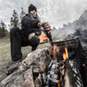 Person using a multi-tool to cook over a campfire outdoors.

