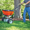 Person using a push spreader to fertilize a lawn.

