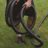 Person installing flexible black PVC pipe outdoors on a grassy lawn.
