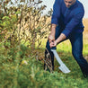 Person using a large machete to clear brush outdoors.
