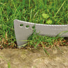 Silver billhook saw blade cutting through grass near ground.
