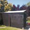 Black knitted shade tarp covering RV, providing sun protection in backyard setting.
