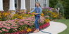 Woman watering vibrant garden flowers with extendable hose.

