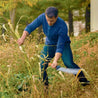 Man using a machete to clear overgrown vegetation in an autumnal garden.
