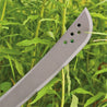 Close-up of a 24-inch machete blade amidst lush green vegetation.
