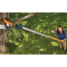 Extendable pole saw pruning high branches in a garden.
