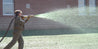 Person applying bonded fiber matrix to a lawn using a specialized sprayer near a brick building.

