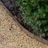 Rustic steel garden edging installed beside gravel and greenery.
